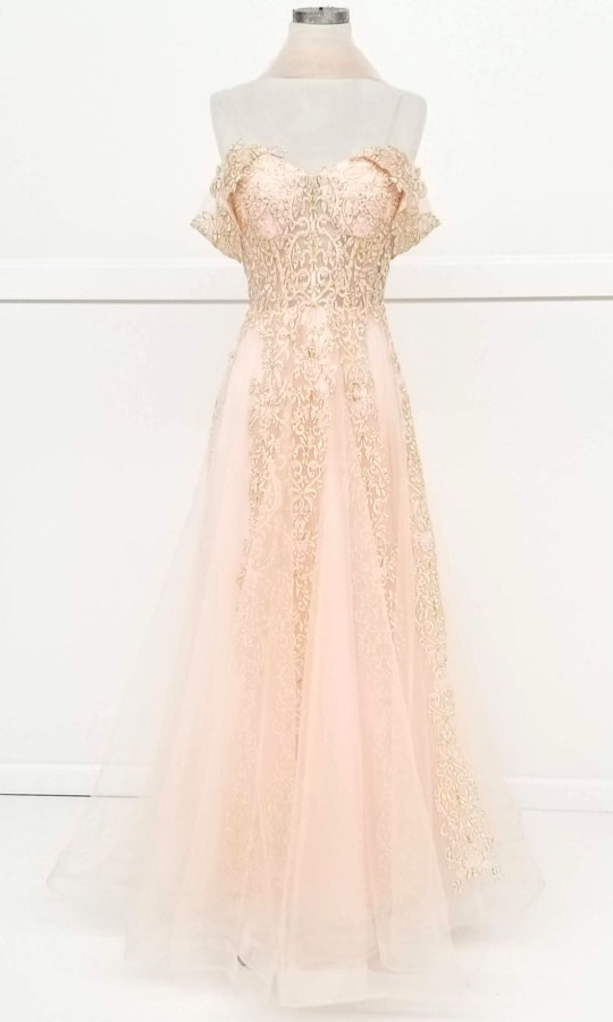 The Long Lace Prom Ball Gown: Chicas CA1103 is an off-the-shoulder light pink dress with gold lace on the bodice and a flowing tulle skirt, shown on a dress form against a white background.